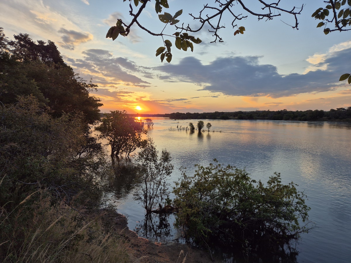 Golden sunset over a wide river, framed by trees on the bank