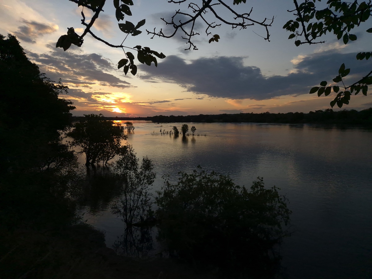 Sun breaking through cloud over a river, with silhouetted trees