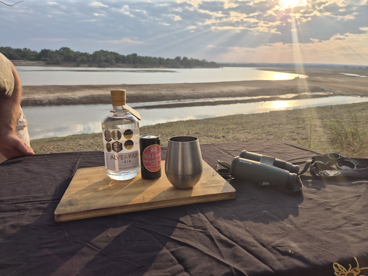 Sundowners with gin, tonic and binoculars overlooking a wide river at sunset