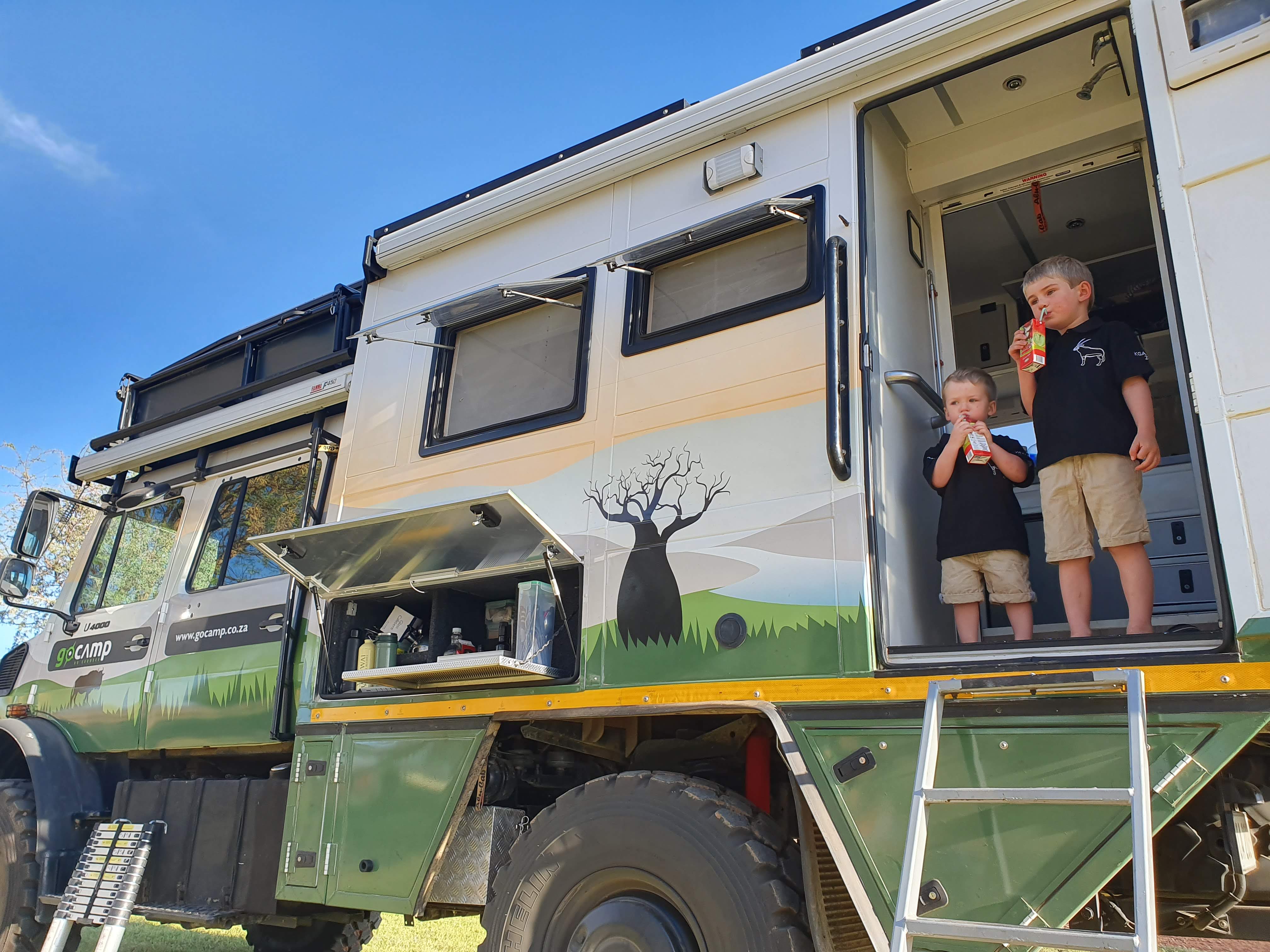Two boys in the doorway of an expedition truck, juice boxes in hand