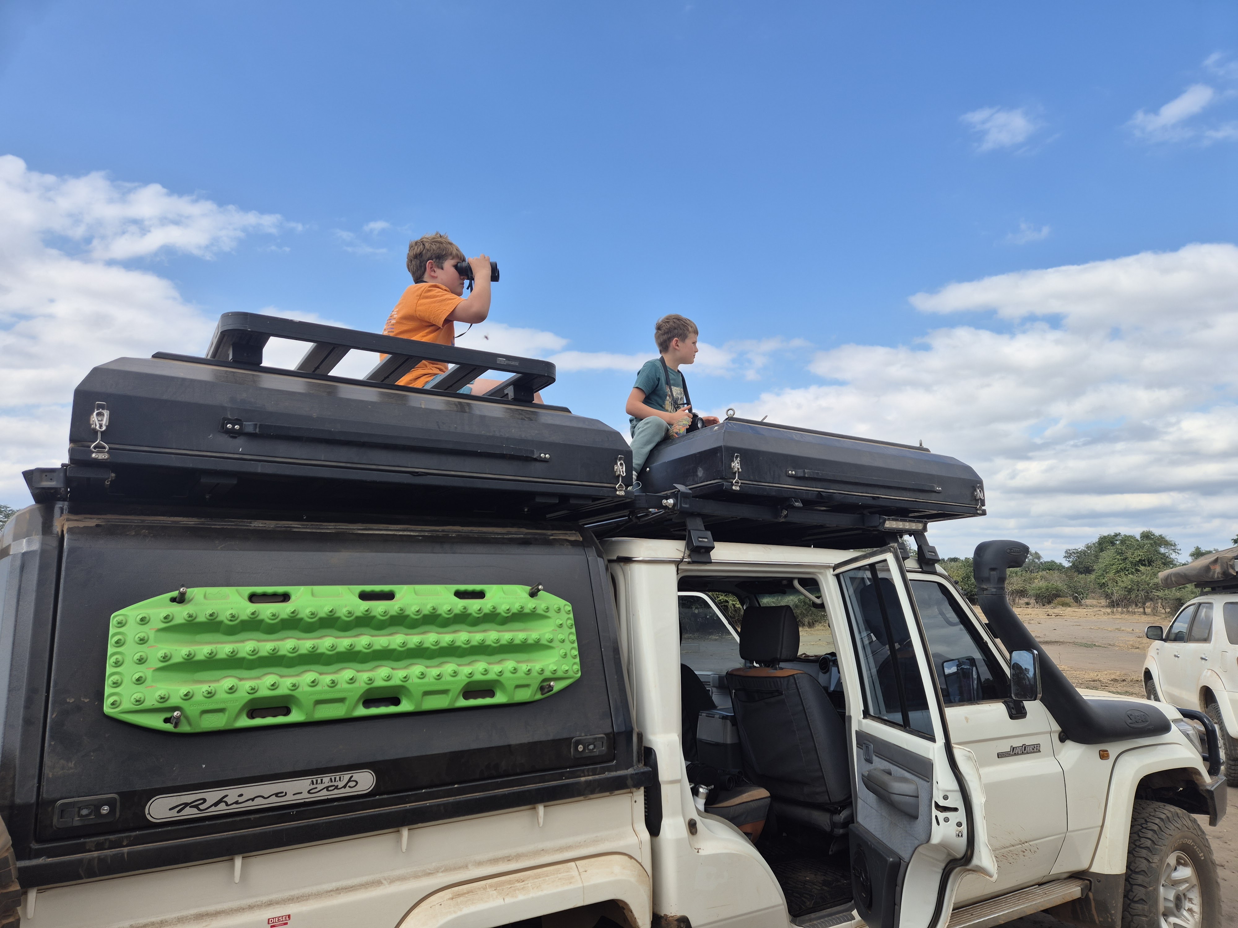 Two boys sitting on rooftop tents of a Marula 4x4, looking out over the savanna