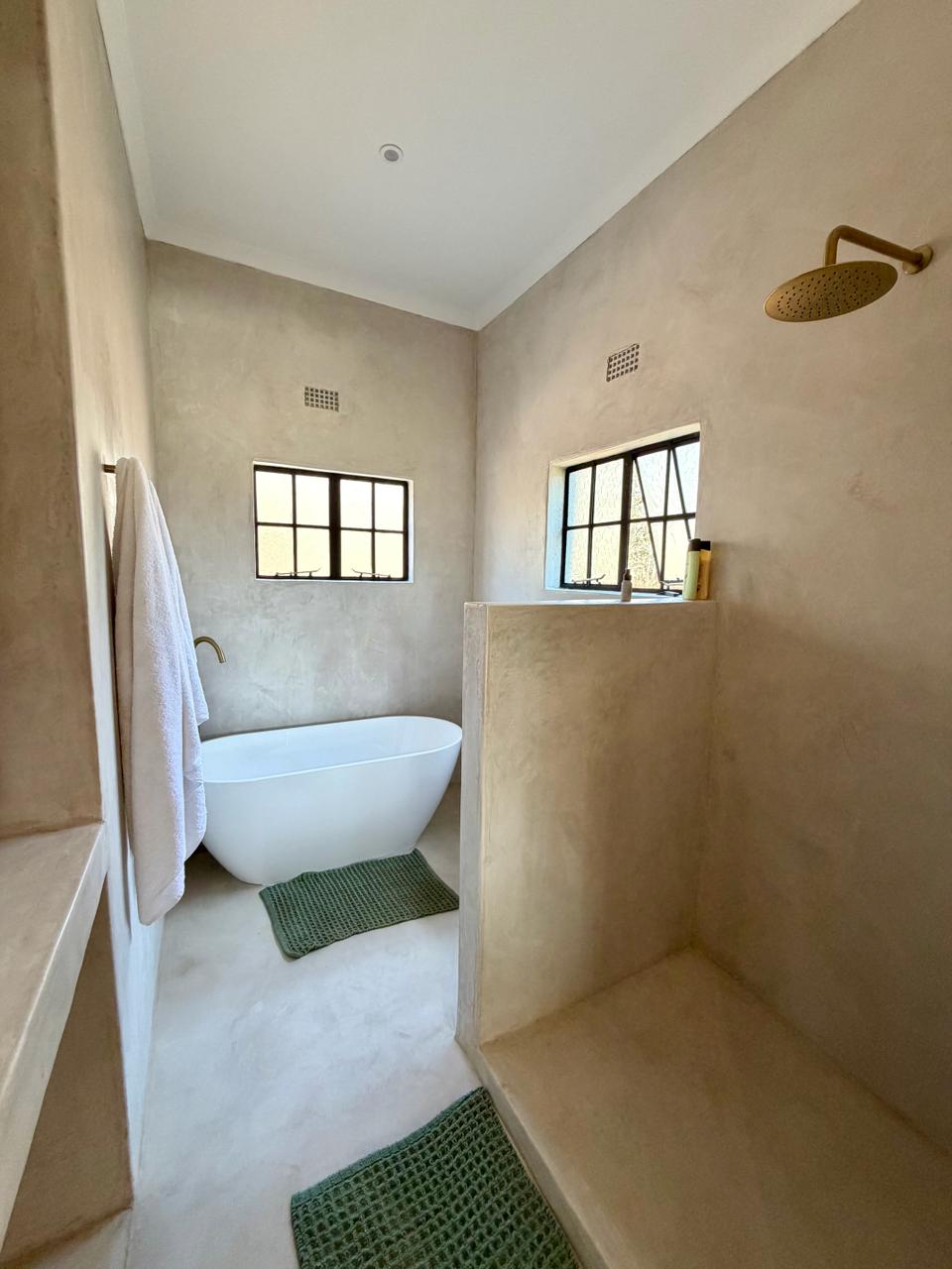 A sand-plastered bathroom with a freestanding bath and rain shower