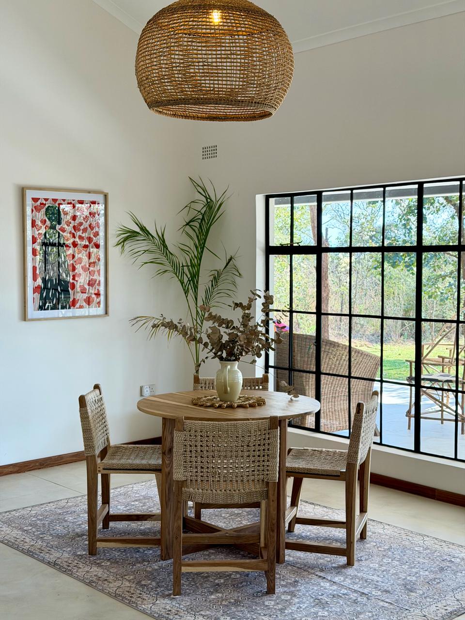 A round wooden dining table beneath a woven pendant light