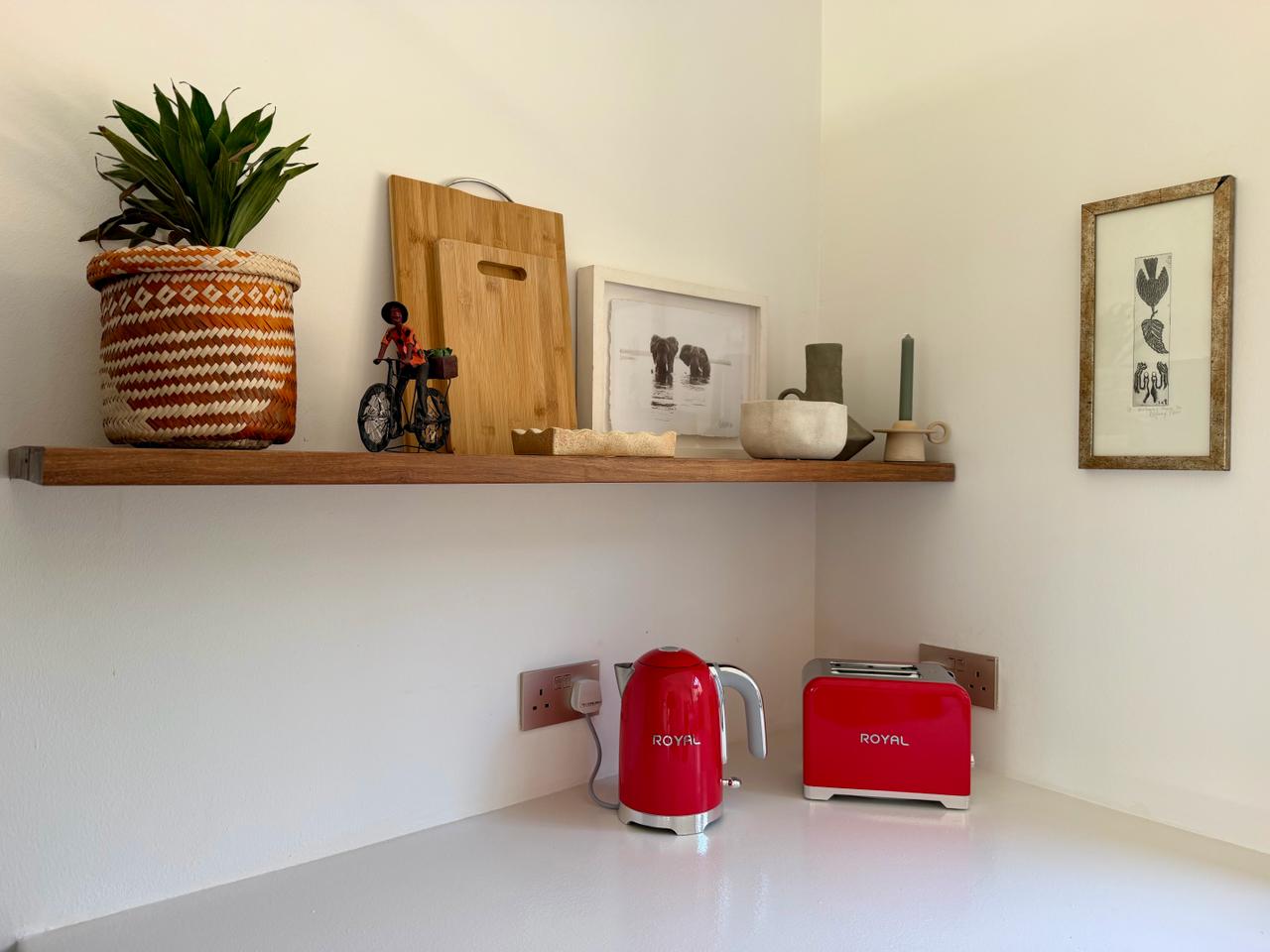 Red kettle and toaster on the kitchen counter beneath a wooden shelf