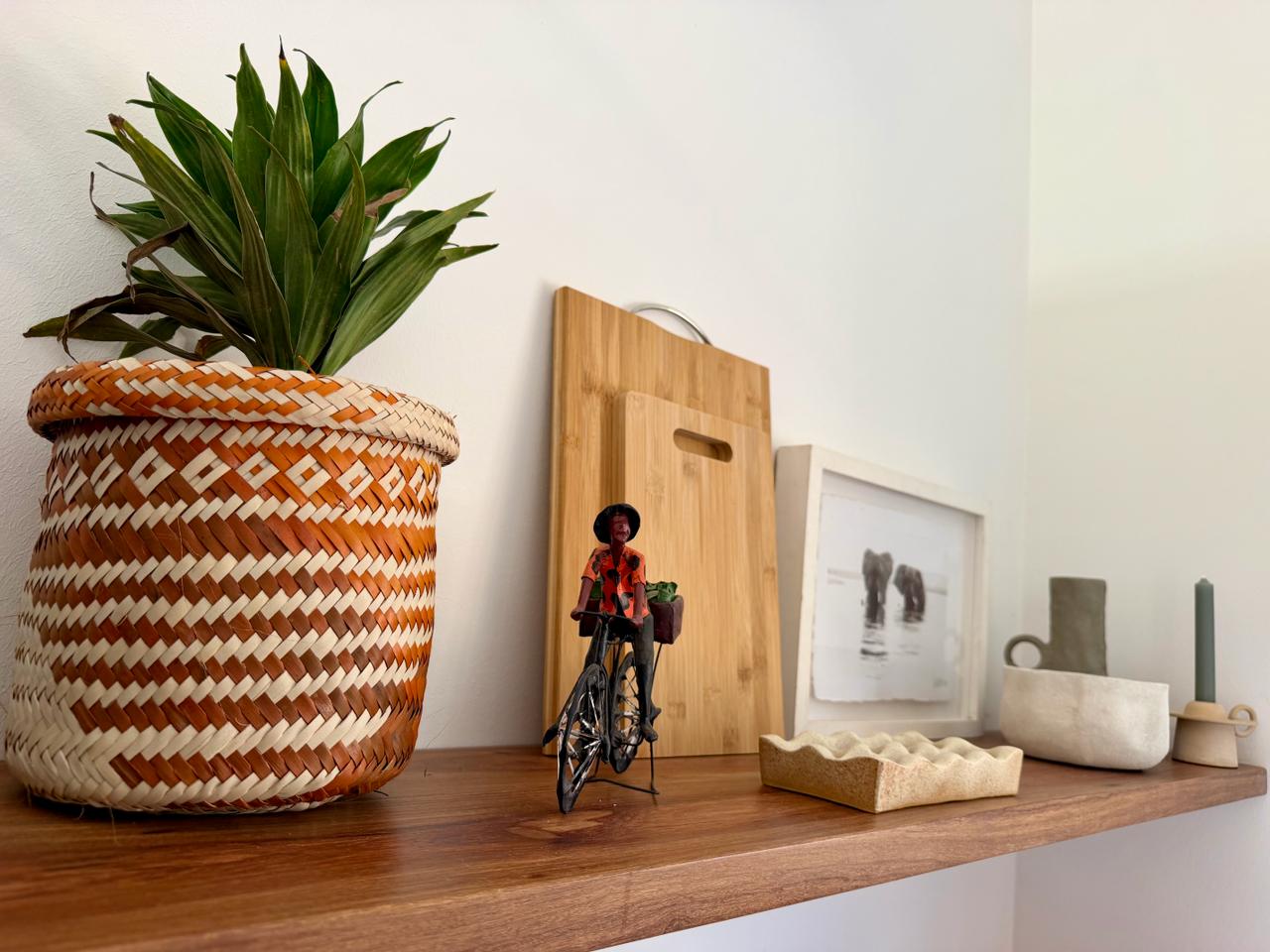 A wooden shelf with a plant, ceramics and a small print of elephants