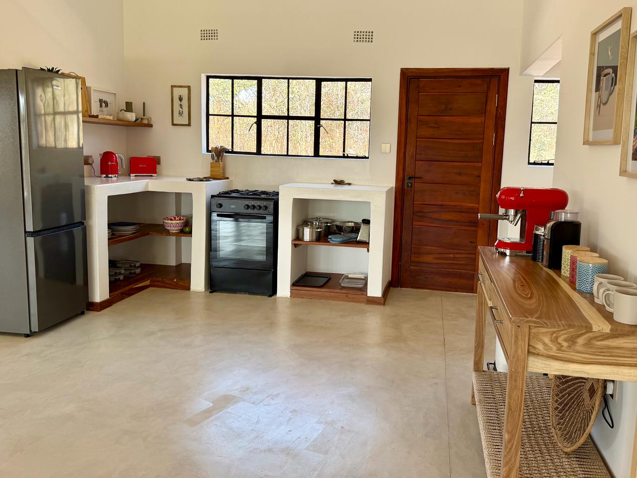 The cottage kitchen, with a gas stove, open wooden shelves and a view of the trees