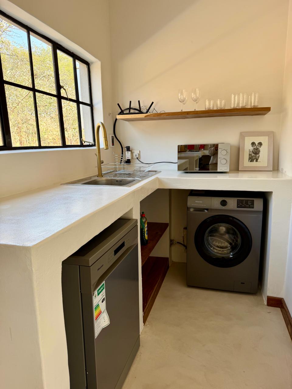 The utility area, with a sink, dishwasher, washing machine and a window to the trees