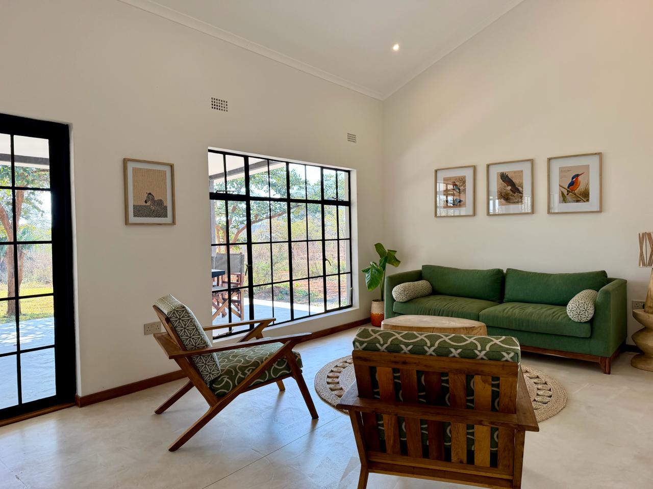 The living room, with a green sofa, wooden armchairs and bird prints on the wall