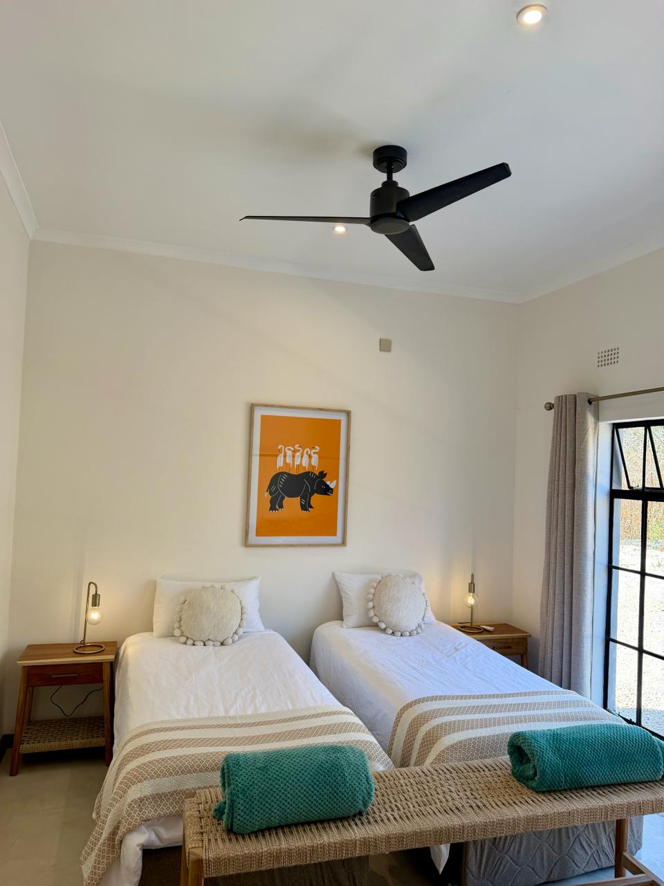 Twin beds with a rhino print above and a ceiling fan overhead